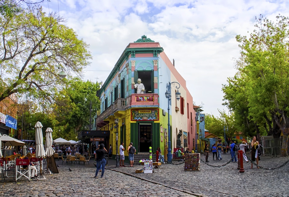 Buenos Aires, Argentina - April 15, 2015: The main square on of the Camanito in the La Boca neighborhood of Buenos Aires features brightly colored buildings and cobblestone streets that are a popular tourist destination. Tourists can be seen surrounding the most recognizable building the the neighborhood at the center of the square. The area is a popular destination for watching tango dancers in the street, shopping for souvenirs handicrafts made by local artisans and restaurants. It is the oldest neighborhood in Buenos Aires and is located at the mouth of the port, which gives it its namesake.